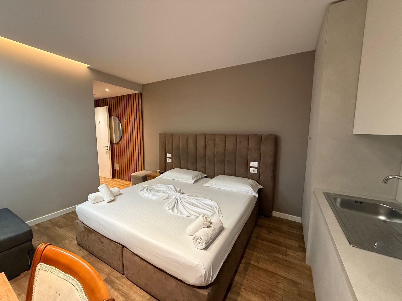 A hotel room with a bed, a desk, a chair, a bathroom, and a kitchenette.