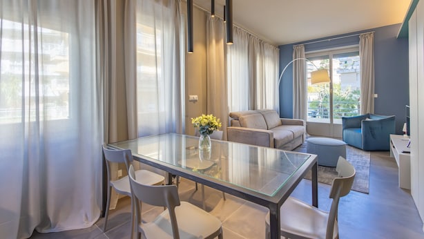 A modern living room with a glass dining table, beige sofa, and a blue armchair. - Sanremo Belle Epoque Apartment by Wonderful Italy (Sanremo)