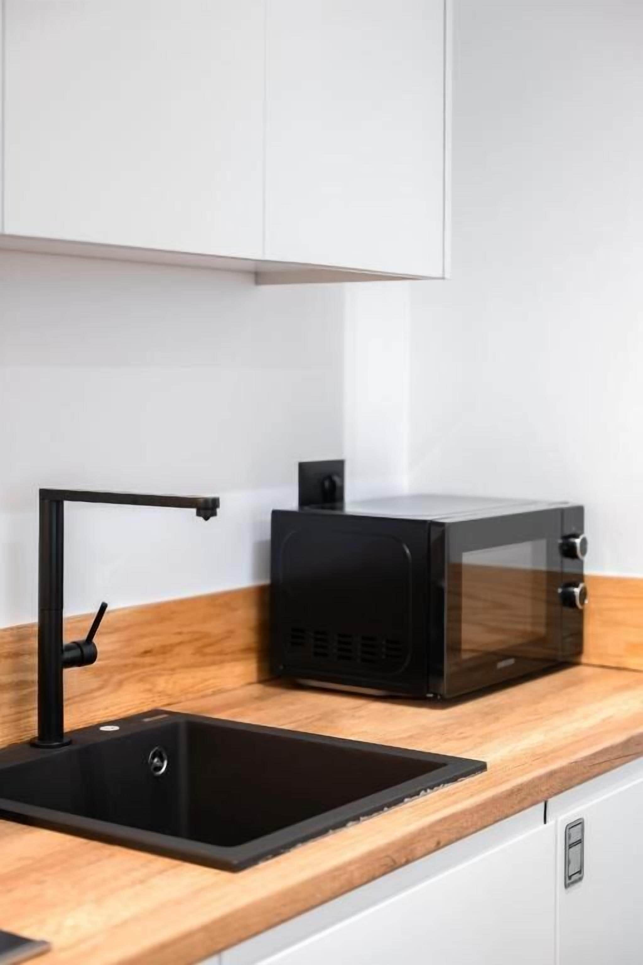 Une cuisine avec un évier noir, un four à micro-ondes et un plan de travail en bois.