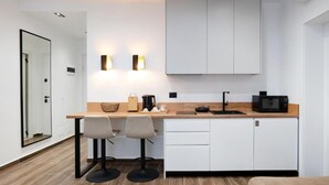 Una cocina moderna con armarios blancos, encimera de madera, dos taburetes de bar, un microondas y una cafetera.