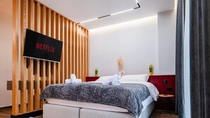 Habitación de hotel moderna con pared de listones de madera, cama con manta de diseño gris, televisor de pantalla plana montado en la pared y una mesita de noche con una planta.
