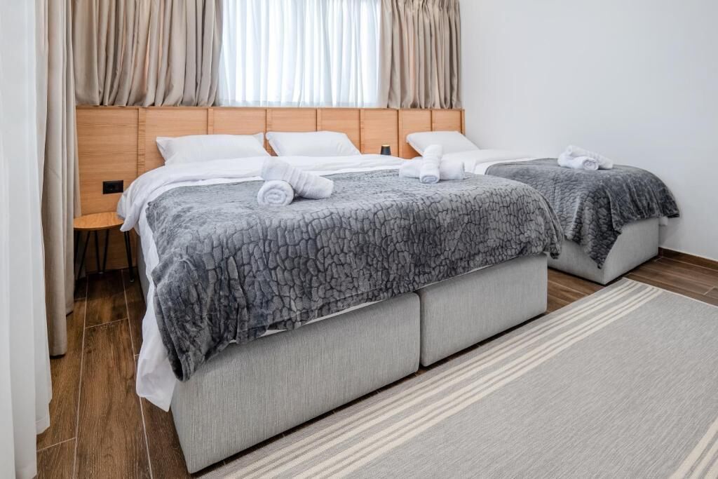 A double bed with grey patterned bedding and two pillows, a wooden headboard, and a small bedside table.