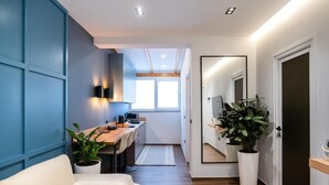 Habitación de hotel moderna con sofá, escritorio con ordenador, espejo y plantas en macetas.