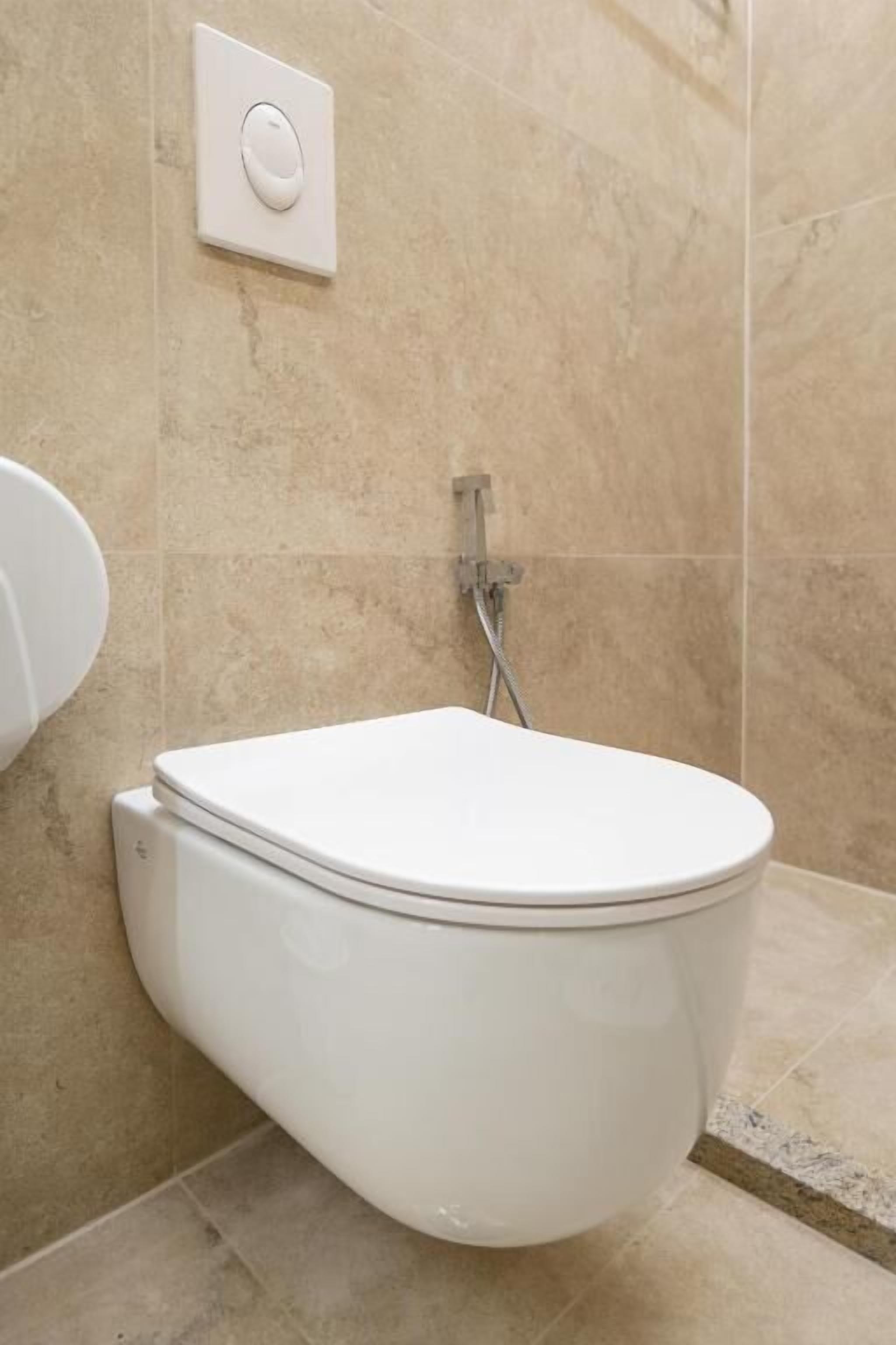 A modern bathroom with a wall-mounted toilet, a showerhead, and a flush control panel.