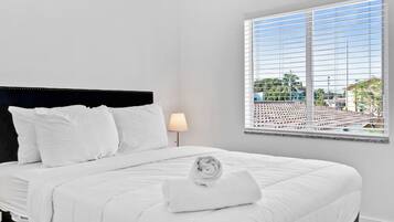 Ein Hotelzimmer mit einem Bett, weißer Bettwäsche, einer Lampe und einem Fenster mit Jalousien.