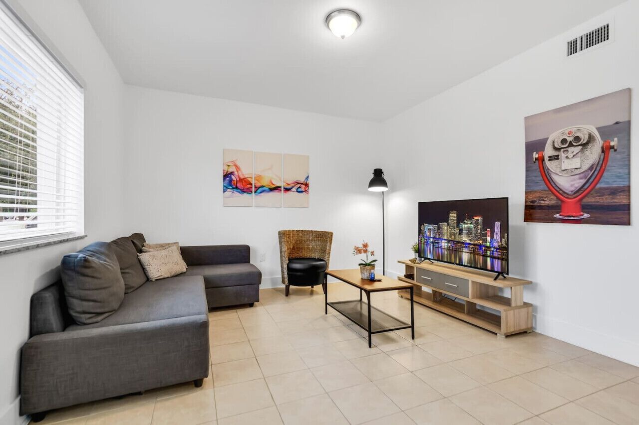 A modern living room with a grey sofa, a black chair, a wooden coffee table, and a TV on a wooden stand.