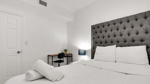 Ein Hotelzimmer mit einem großen Bett, einem gepolsterten Kopfteil, einem Schreibtisch mit Stuhl, einer Lampe und einer Tür.