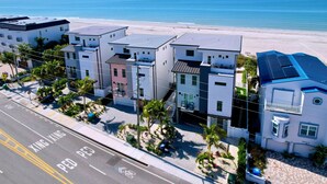 A coastal residential area with modern buildings, a clear sky, and a beach in the background. - Beach Two: Style Meets the Shore w/ Pool and Spa (Treasure Island)