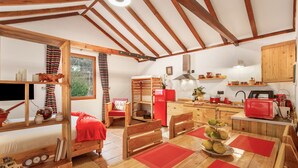 A cozy, rustic room with a wooden bed, a dining table with red placemats, a kitchen area with a red refrigerator, and a wooden ceiling. - Vacation Apartment 'Casa Rural Ruta Del Tajinaste Azul' with Sea View, Wi-Fi & Air Conditioning (Valsequillo)