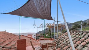 A terrace with a table and chairs, a green metal structure, and terracotta roof tiles. - Vacation Apartment 'Casa Rural Ruta Del Tajinaste Azul' with Sea View, Wi-Fi & Air Conditioning (Valsequillo)