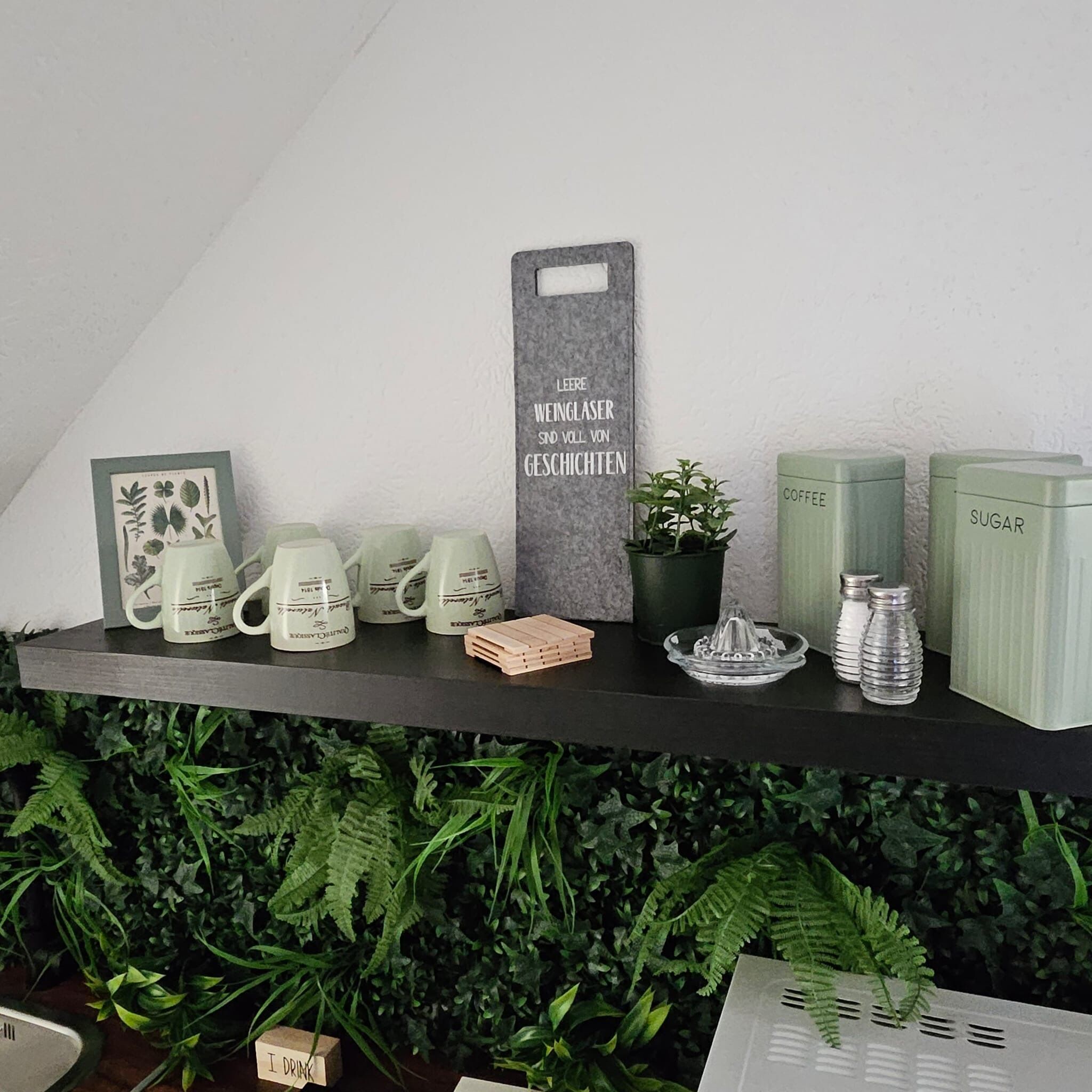 Una estantería con diversos objetos, incluyendo tazas, una cafetera, un azucarero y un cartel con texto.