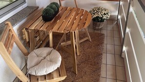 Une table et des chaises en bois sont posées sur un tapis tissé, avec une petite plante en pot et un panier accroché au mur.