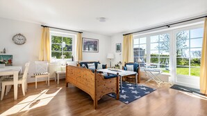 Ein geräumiges Zimmer mit einem hölzernen Bett, einem Esstisch, Stühlen und großen Fenstern mit Blick auf Grünflächen.