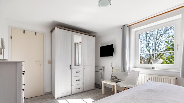 Ein Schlafzimmer mit Bett, Schreibtisch, Stuhl, Kleiderschrank, Fernseher und einem Fenster mit Blick.