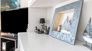Ein modernes Wohnzimmer mit Flachbildfernseher, einem gerahmten Spiegel, dekorativen Enten, einer Lampe und einem kleinen Modell eines Segelboots.