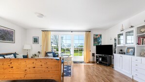 Ein geräumiges Zimmer mit einem Holzbett, einem Fernseher, einem Schreibtisch und Blick durch große Fenster.
