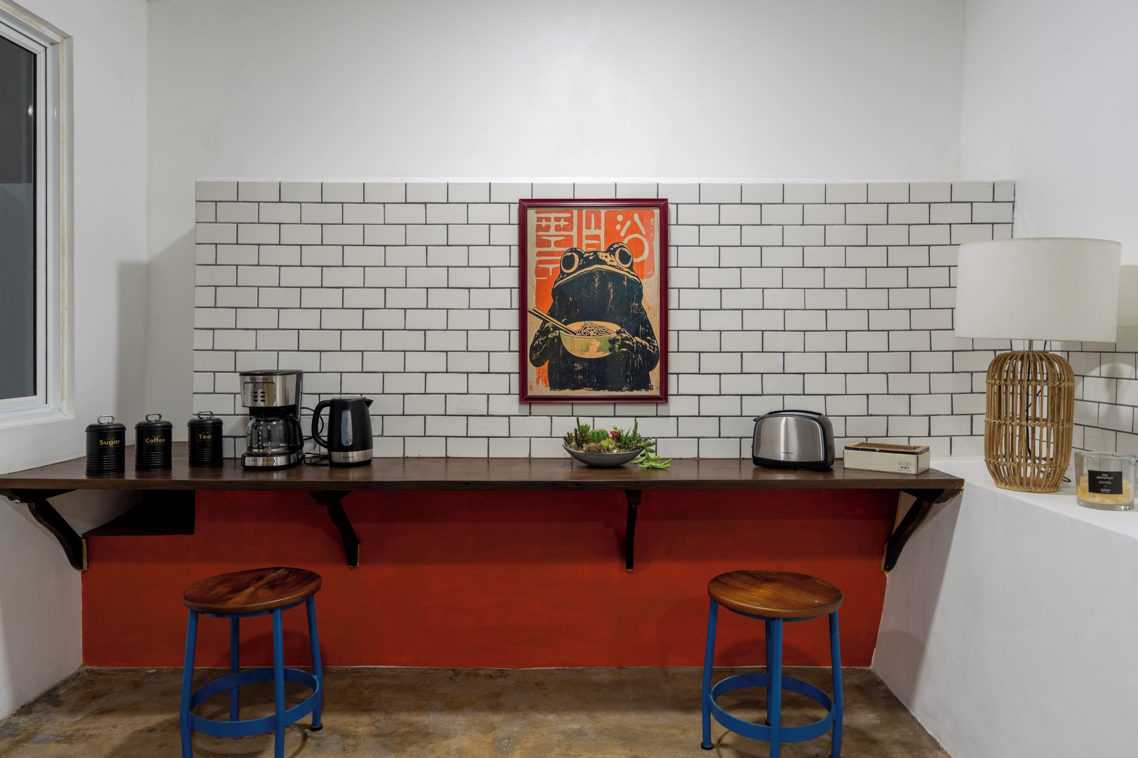 A kitchen with a white brick backsplash, a coffee maker, a kettle, a toaster, and two stools.