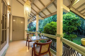 A covered outdoor seating area with a table and chairs, a hanging light fixture, and a view of lush greenery.