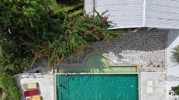 Vista aérea de um hotel com piscina, cercado por vegetação exuberante e um caminho de pedra.