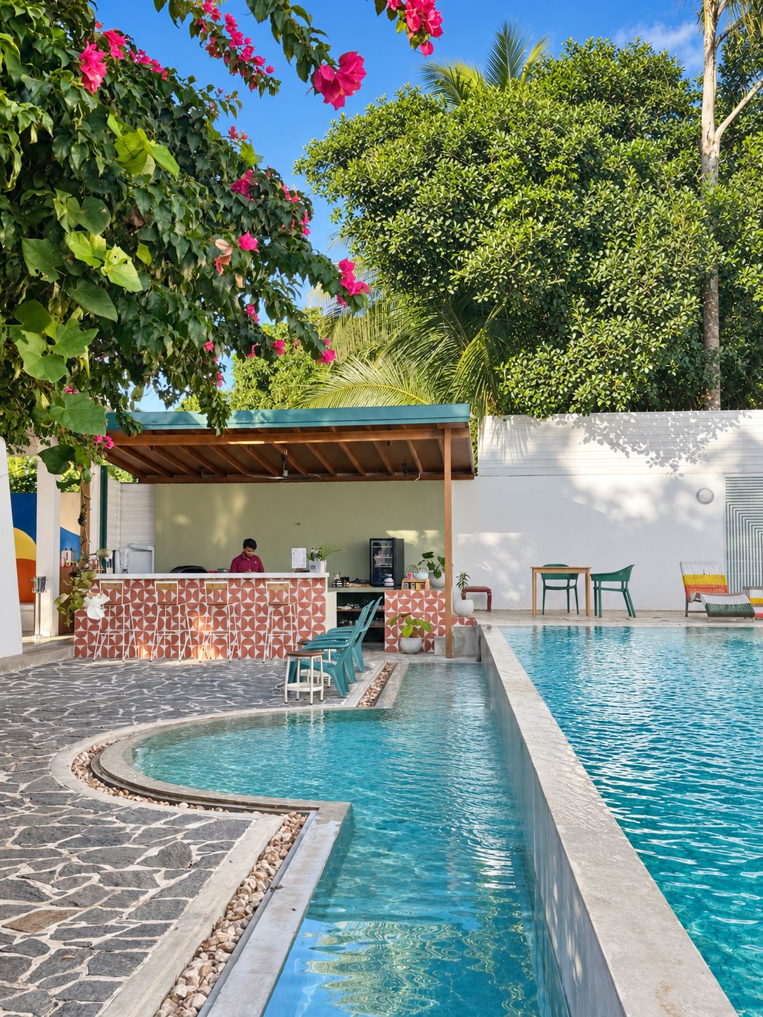 A swimming pool with a stone border, a covered seating area, and a bar with a patterned wall.