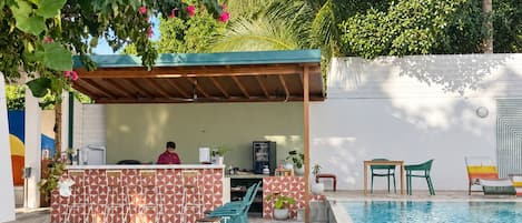 A swimming pool with a stone border, a covered seating area, and a bar with a patterned wall.