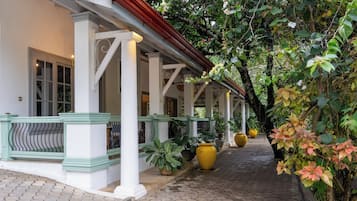 A covered walkway with columns, potted plants, and a bench.