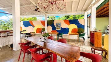 A dining area with a wooden table and red chairs, a ceiling fan, and a colorful mural on the wall.