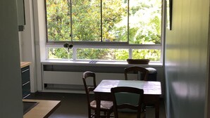 A compact kitchen with a dining table and chairs, a window with a view of greenery, and a pendant light. - Spacious, bright apartment near Paris (Louveciennes)