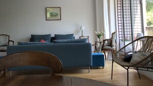 A modern living room with a blue sofa, wooden coffee table, and wicker chairs. - Spacious, bright apartment near Paris (Louveciennes)