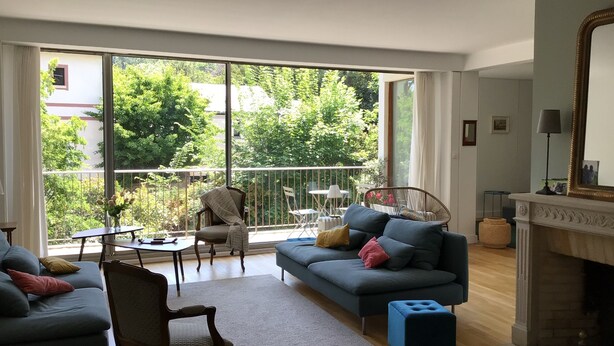 A spacious living room with a large window, a sofa set, a chair, a small table, and a fireplace. - Spacious, bright apartment near Paris (Louveciennes)