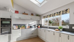 A modern kitchen with white cabinetry, a skylight, and a window with a leaf-patterned valance. - Newlands (Yelverton)
