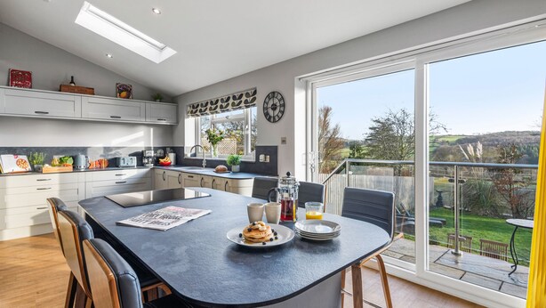 A modern kitchen with a large island, white cabinetry, and a view of the outdoors. - Newlands (Yelverton)