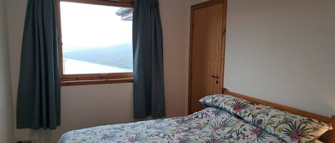 A bedroom with a bed, a window with curtains, and a door.