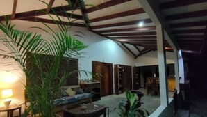 Amplia sala de estar con techo alto, vigas de madera, un sofá, una mesa de comedor y varias plantas.