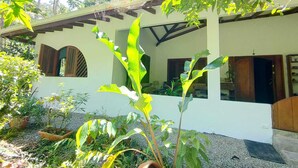 Una casa con porche cubierto, ventanas amplias y un jardín con diversas plantas.