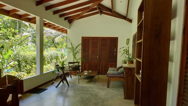 Una habitación con techo de madera, un ventanal grande, un sofá, una silla y una estantería.