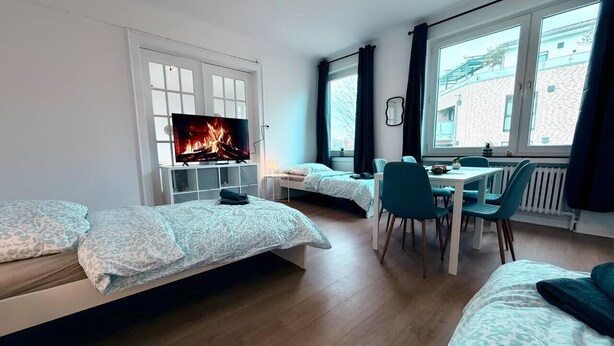 A modern room with two beds, a TV, a dining area, and large windows. - sleepWELL-Nordhorn - Large & modern central location (Nordhorn)