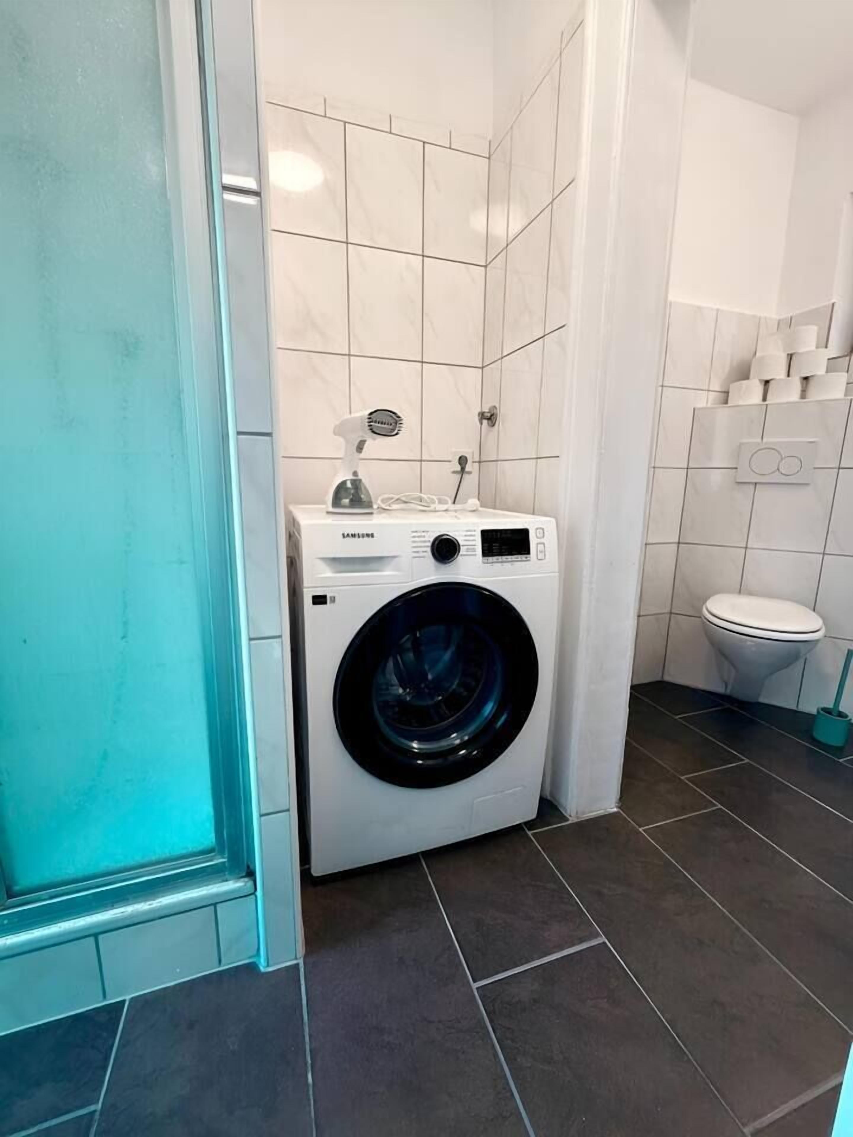 A compact laundry room with a front-loading washing machine, a small sink, and a toilet.