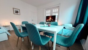 A modern room with a dining table and chairs, a TV with a fireplace image, and a bed with a blue bedspread. - sleepWELL-Nordhorn - Large & modern central location (Nordhorn)