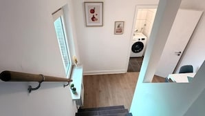 A staircase leading to a laundry room with a washing machine and dryer, a small window, and a door with a coat rack. - sleepWELL-Nordhorn - Large & modern central location (Nordhorn)