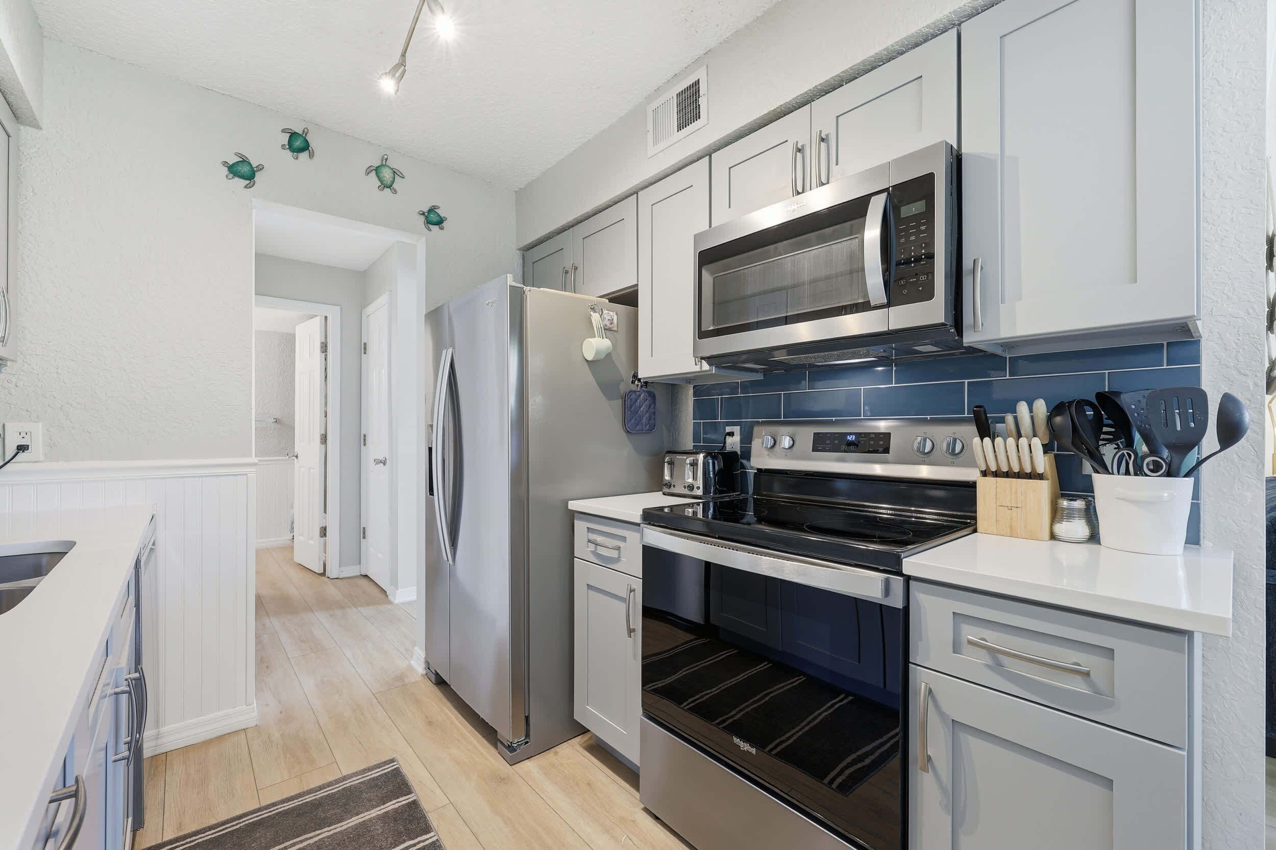 A modern kitchen with stainless steel appliances, white cabinetry, and a blue backsplash.