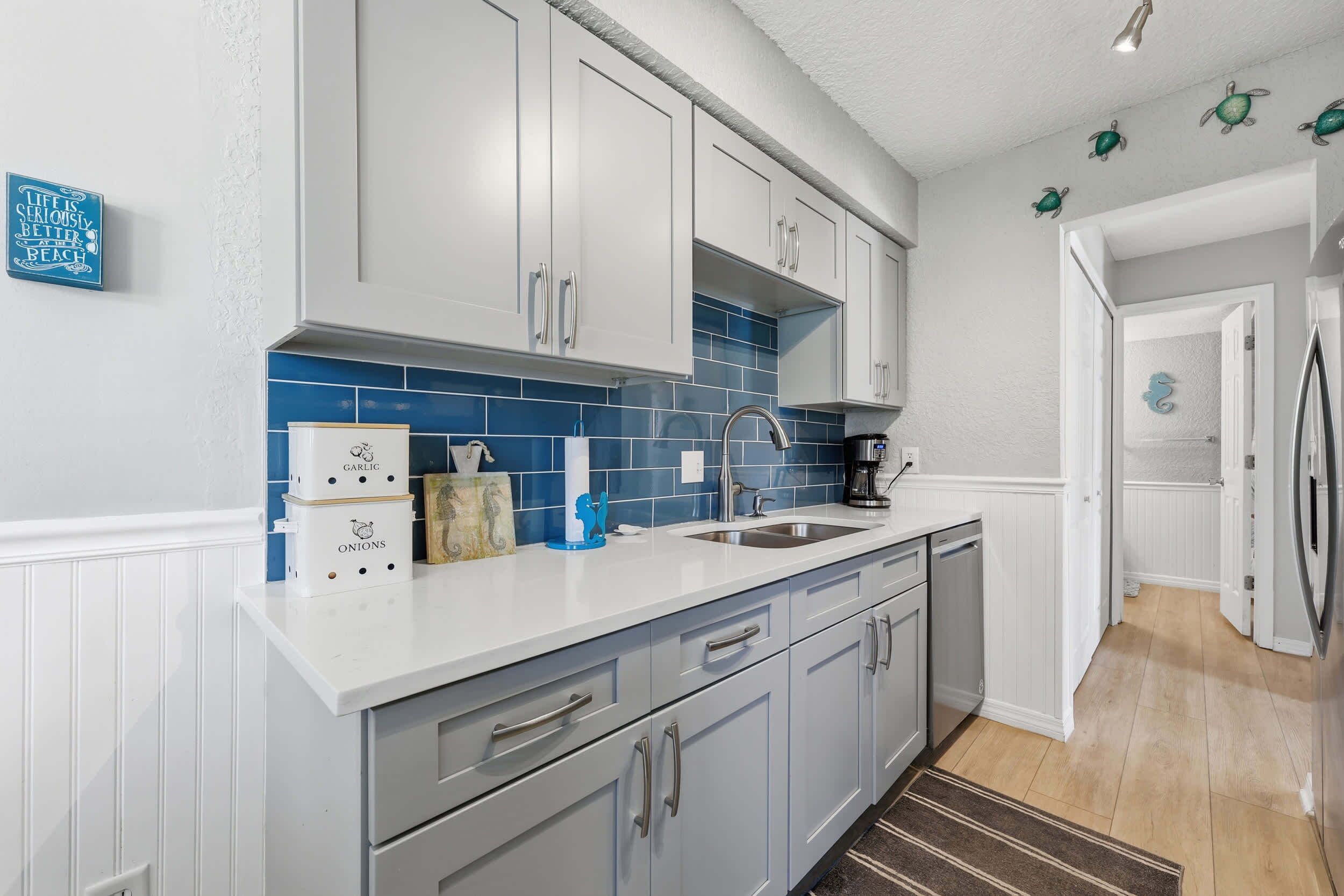 A kitchen with white cabinets, a blue tiled backsplash, and a stainless steel sink.