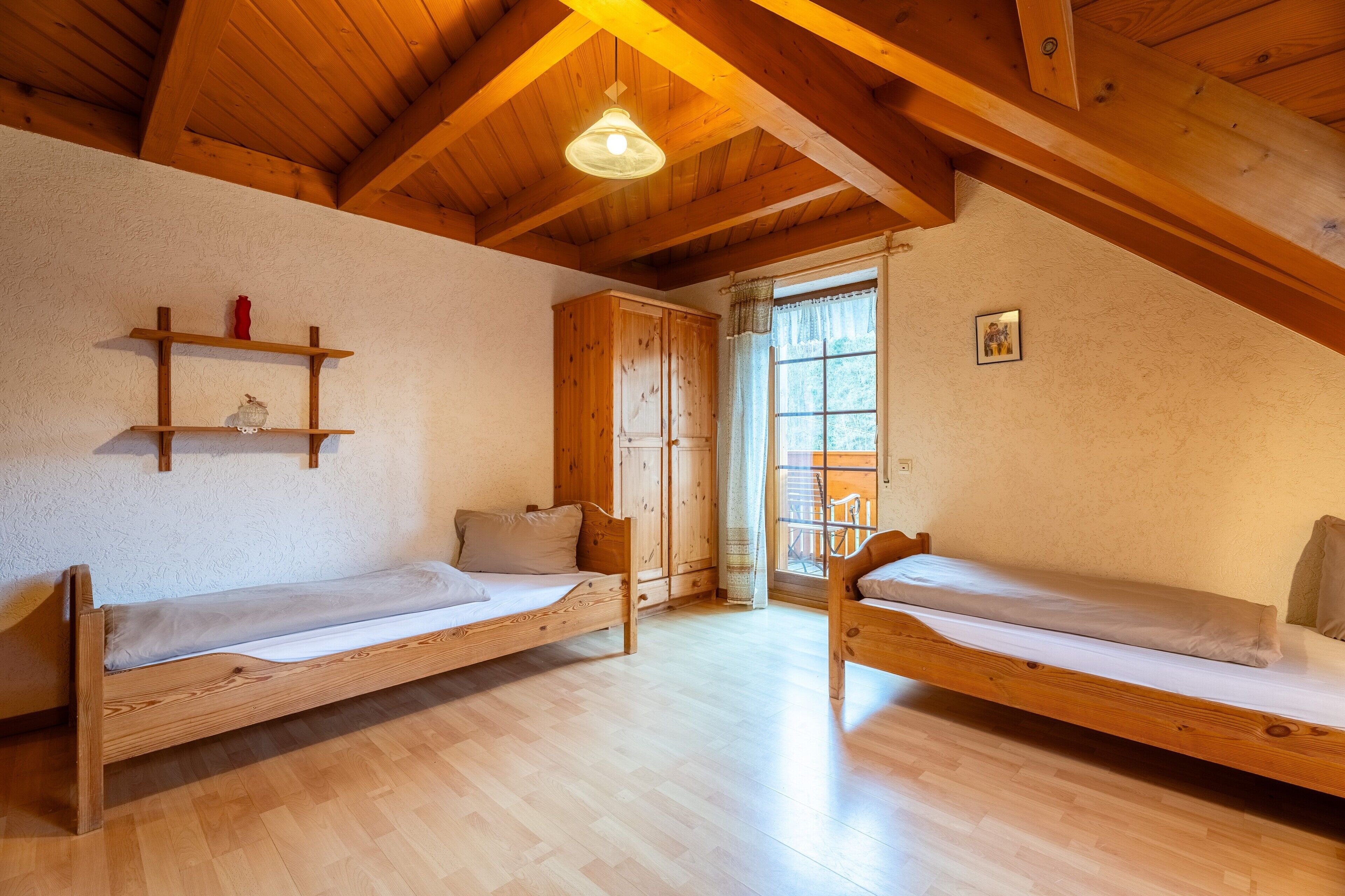 A room with two wooden bunk beds, a wooden ceiling, a window with curtains, and a small shelf with items.