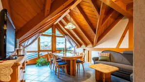 Una habitación acogedora en el ático, con techo de madera, una mesa de comedor con sillas, un sofá y un televisor.