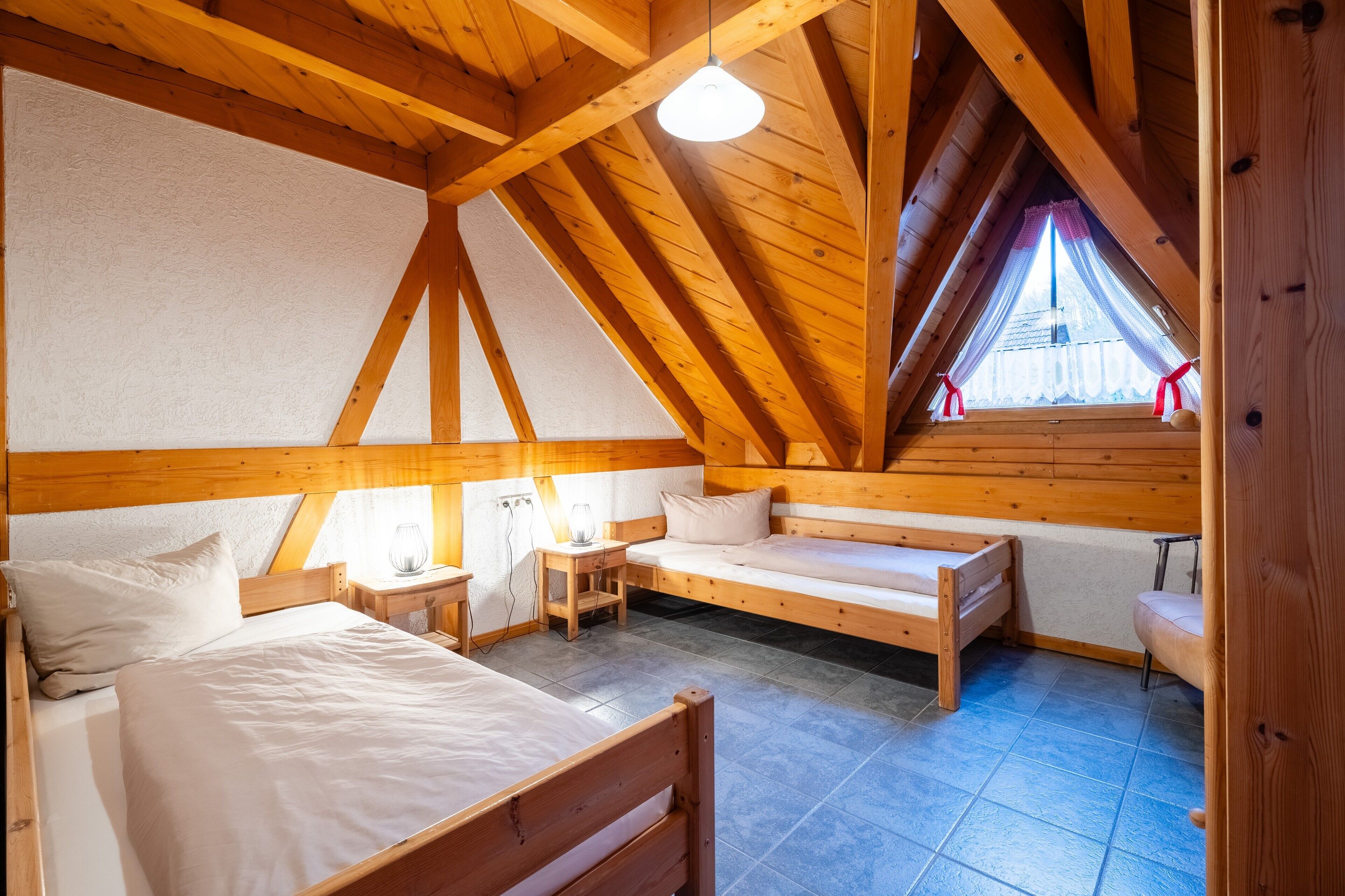 Une pièce avec un plafond en bois, un lit, une petite table avec une lampe et une fenêtre avec des rideaux.