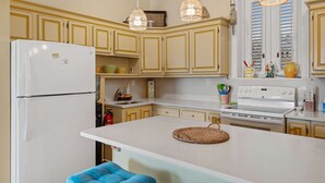 Een keuken met een witte koelkast, een fornuis en een spoelbak. Er zijn houten kastjes en een groot eiland met een geweven placemat.