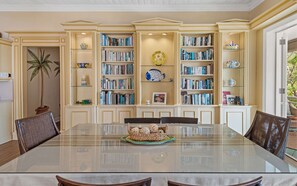 Un comedor con una mesa de vidrio rodeada de sillas, con estanterías a los lados llenas de libros y objetos decorativos.