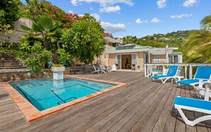 Une terrasse en bois avec une piscine, des chaises longues et un espace salon abrité.