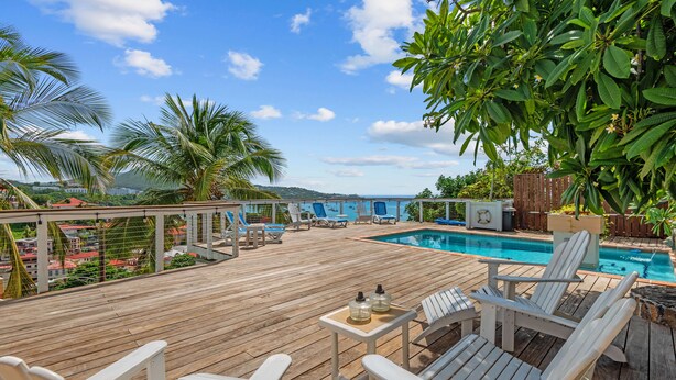 Een houten terras met een zwembad, lounge stoelen en uitzicht op de oceaan.