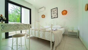 A bedroom with a bed, bedside table, chair, window, air conditioning unit, and artwork. - Residence Jannet 1 Luxury Seaside 3 Bedrooms (Hammamet)